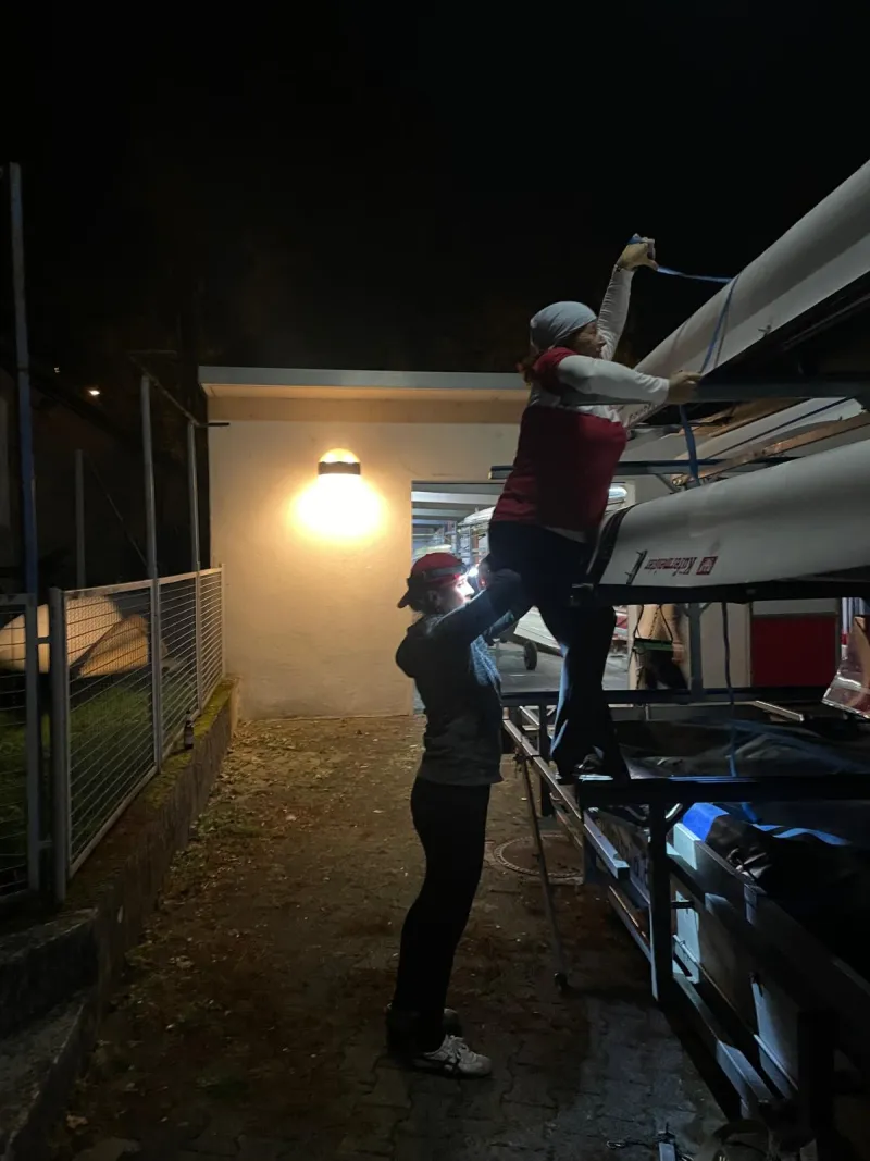 Abends am Bootshaus: zwei Ruderinnen zurren die Boote auf dem Hänger fest