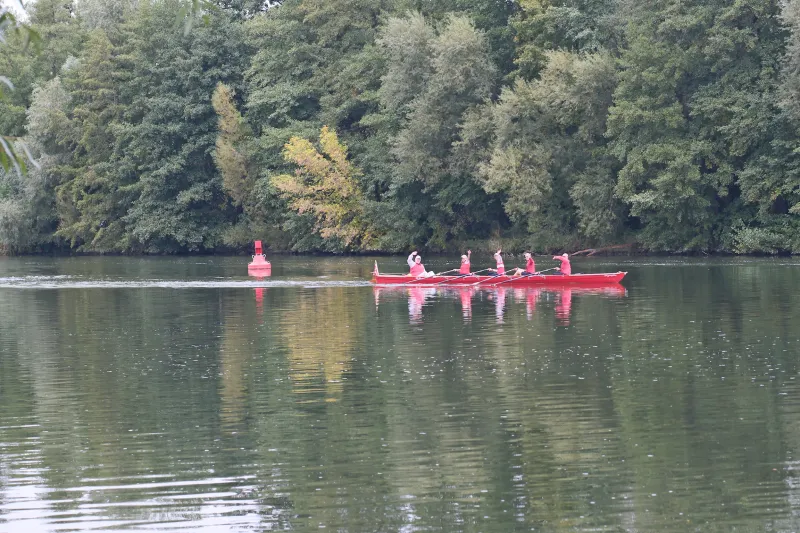 Die Mannschaft winkt vom Boot aus den Radfahrern am Ufer zu