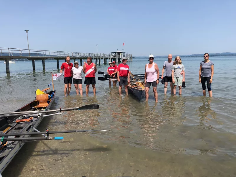 Gruppenfoto der FRGS-Mannschaft im flachen Wasser am Bodensee-Ufer, mit Booten und Steg im Hintergrund